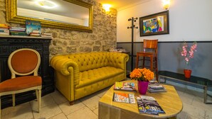 Una sala de estar con un sofá amarillo, una silla de madera, una mesa de centro con revistas, una chimenea y una pared de piedra.