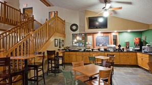 Un restaurante con mobiliario de madera, una escalera, un reloj, un televisor y un letrero en una pizarra.