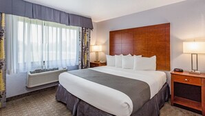 Habitación de hotel con una cama grande, una mesita de noche con lámpara, una ventana con cortinas traslúcidas y aire acondicionado instalado en la pared.