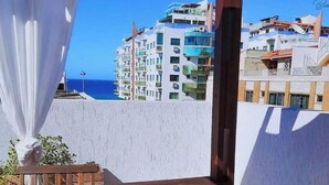 En balkon med et bord dækket til morgenmad, en stol og udsigt til en bygning ved kysten.