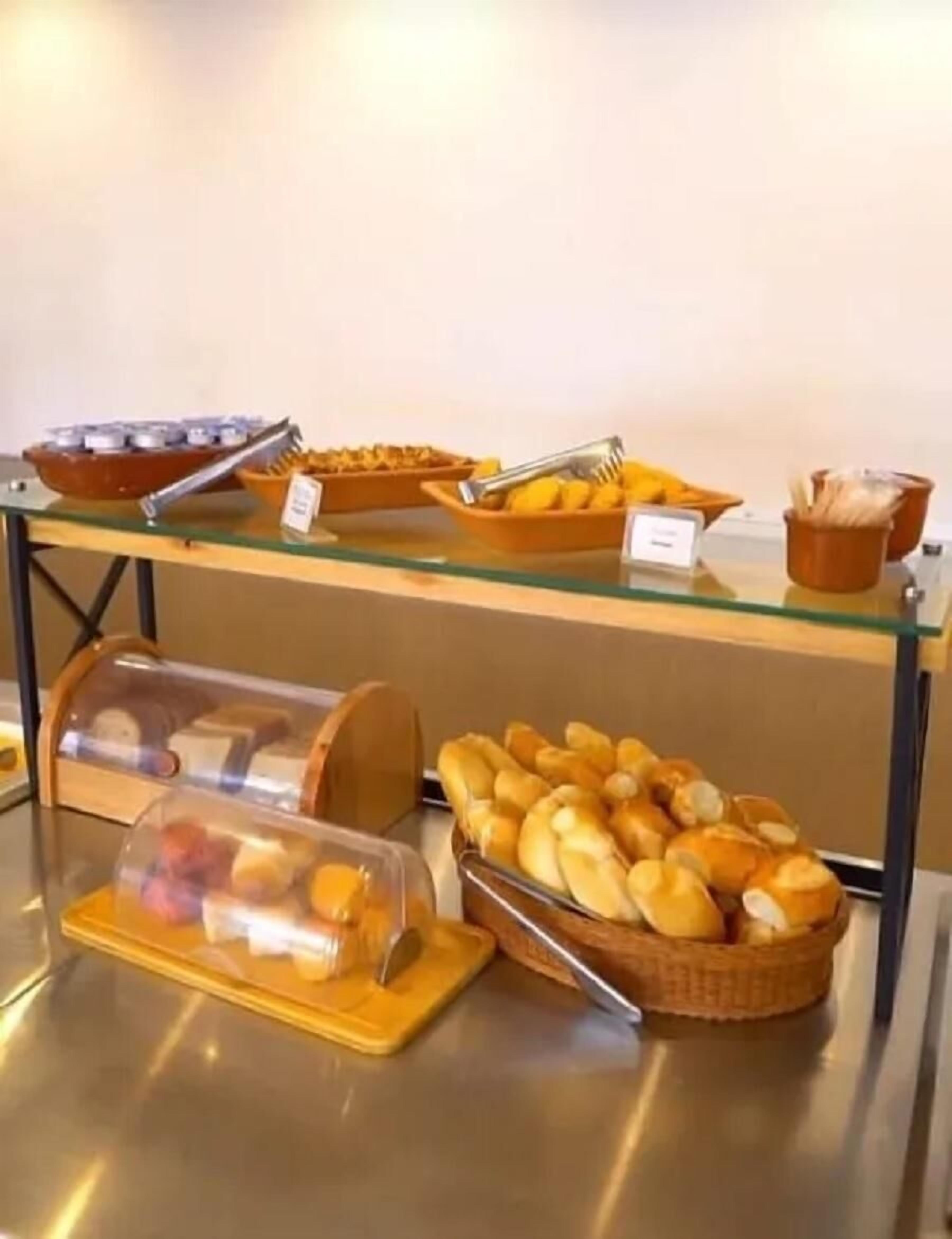 Un bufé con diversos alimentos, entre ellos pan y pasteles, dispuesto sobre una mesa de vidrio.