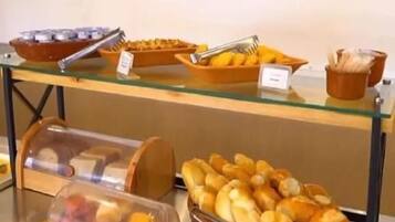 Un bufé con diversos alimentos, entre ellos pan y pasteles, dispuesto sobre una mesa de vidrio.