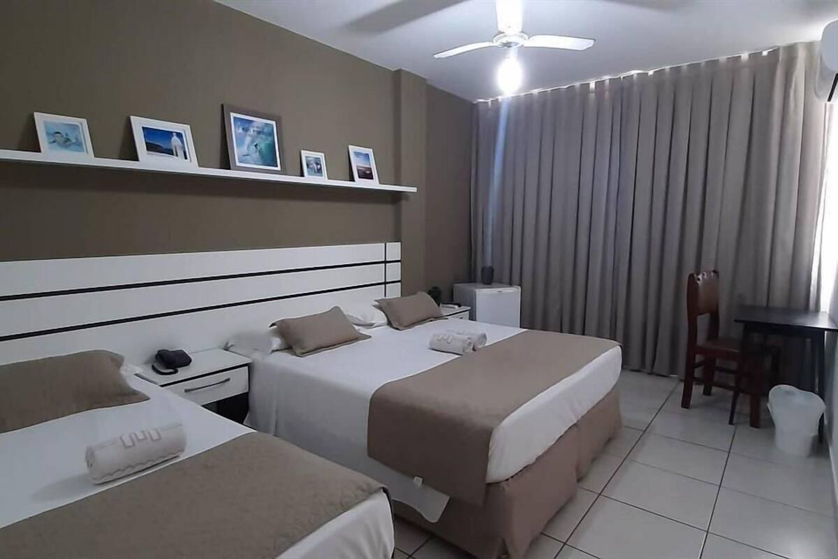 Habitación de hotel con dos camas, un escritorio, una silla, una mesita, una mesita de noche y un ventilador de techo.