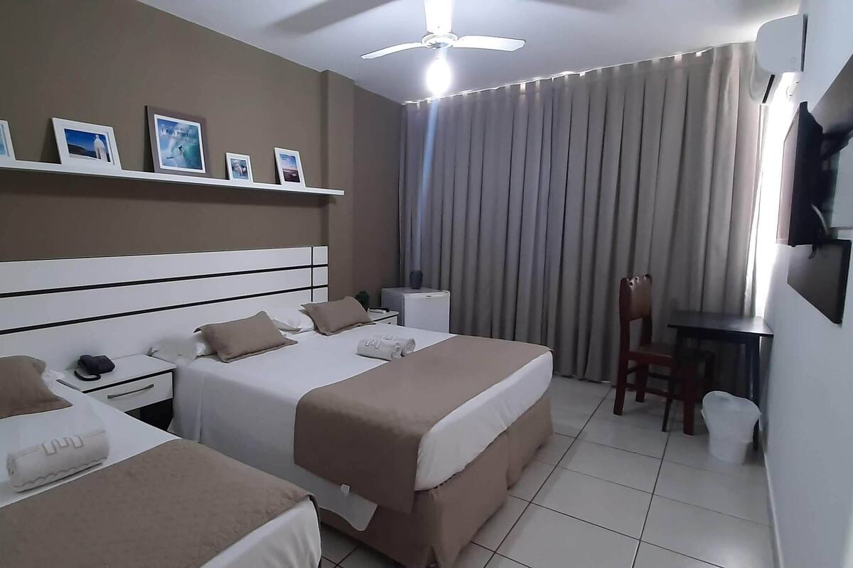 Habitación de hotel con dos camas, un escritorio, una silla, un televisor y un ventilador de techo.