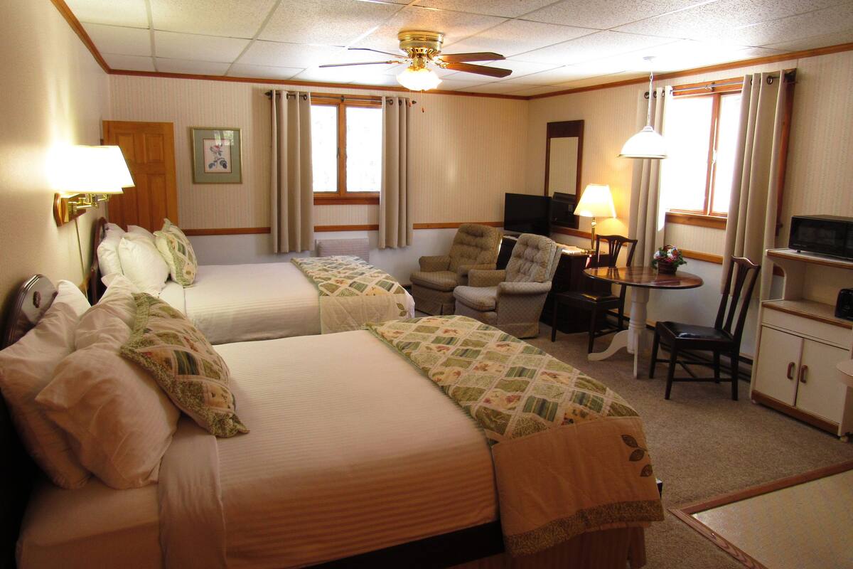 Quarto de hotel com duas camas, uma escrivaninha, uma cadeira, televisão e ventoinha no teto.