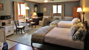 Quarto de hotel com duas camas, uma escrivaninha com cadeira, televisão e ventoinha no teto.