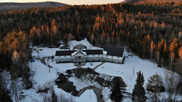 Um edifício grande com várias divisões, rodeado por uma paisagem nevada e uma floresta densa.