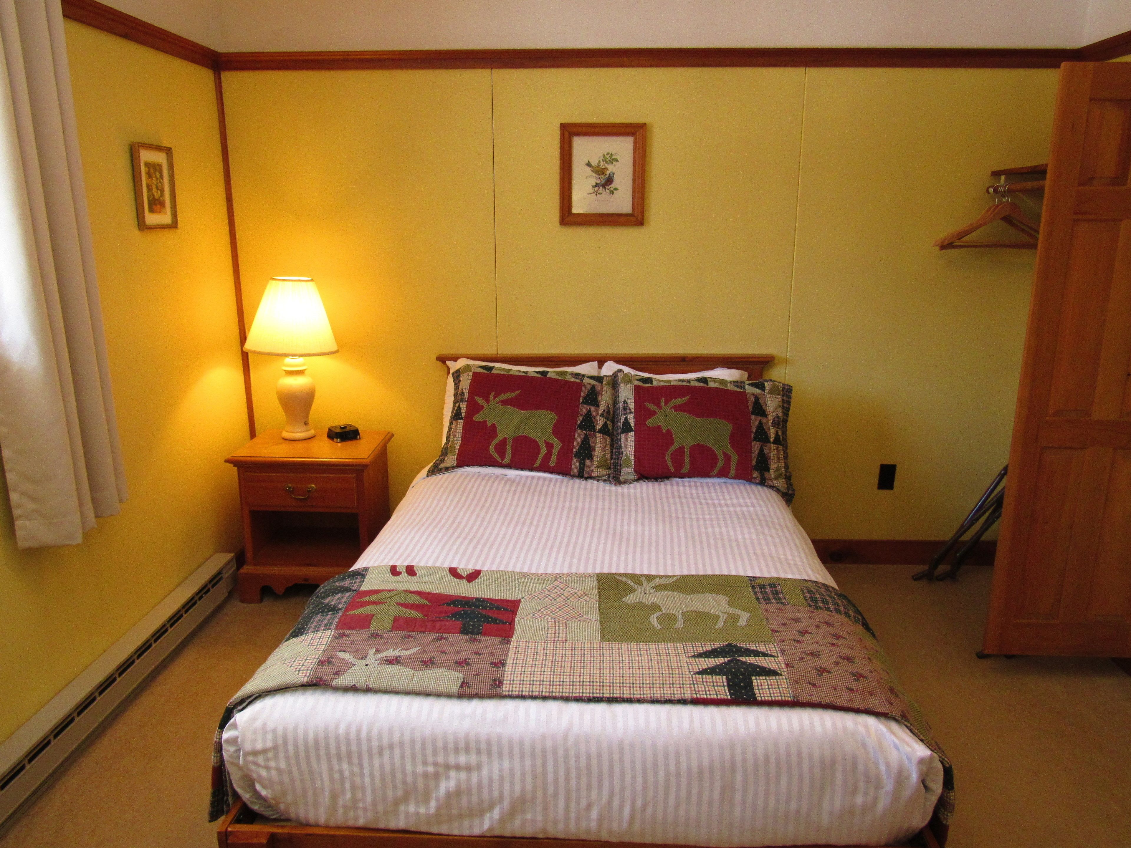 Una cama bien tendida con un edredón a cuadros, una lámpara de noche y un cuadro en la pared.
