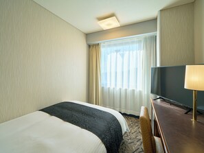 Une chambre d’hôtel avec un lit, une télévision, une lampe et une fenêtre avec des rideaux.