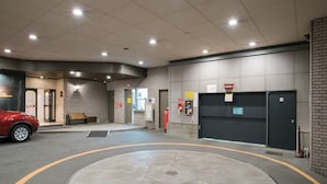 A hotel entrance with a red car parked outside, a roundabout, and a closed garage door.