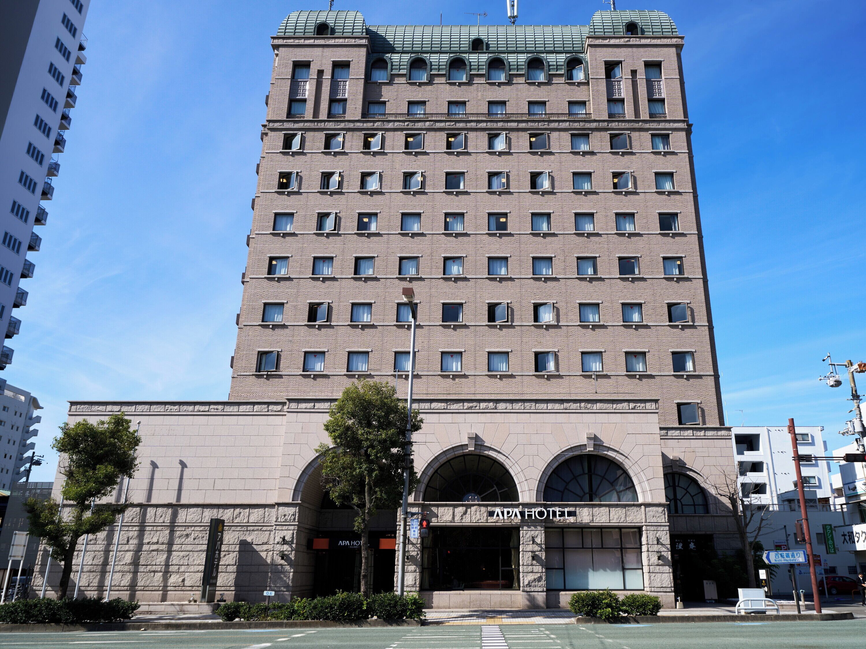 A tall, multi-story building with a prominent entrance featuring arched windows and a sign reading "APA HOTEL".