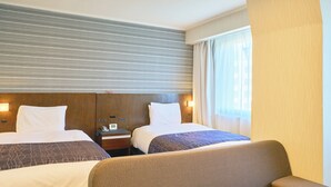 A hotel room with two beds, a sofa, a bedside table with a phone, and a window with curtains.