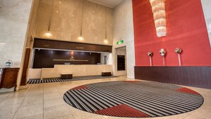 A hotel reception area with a modern design, featuring a large chandelier, a reception desk labeled 'CLOAK', and a patterned carpet.