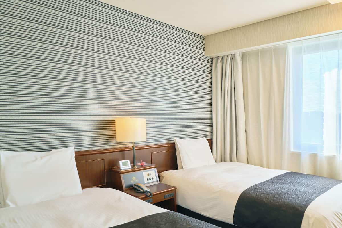 A hotel room with two beds, a bedside table with a lamp, a phone, and a minibar.