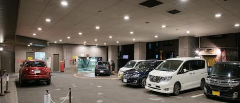 Un espace de stationnement avec plusieurs voitures, un poste de sécurité et une entrée d’immeuble avec une enseigne.