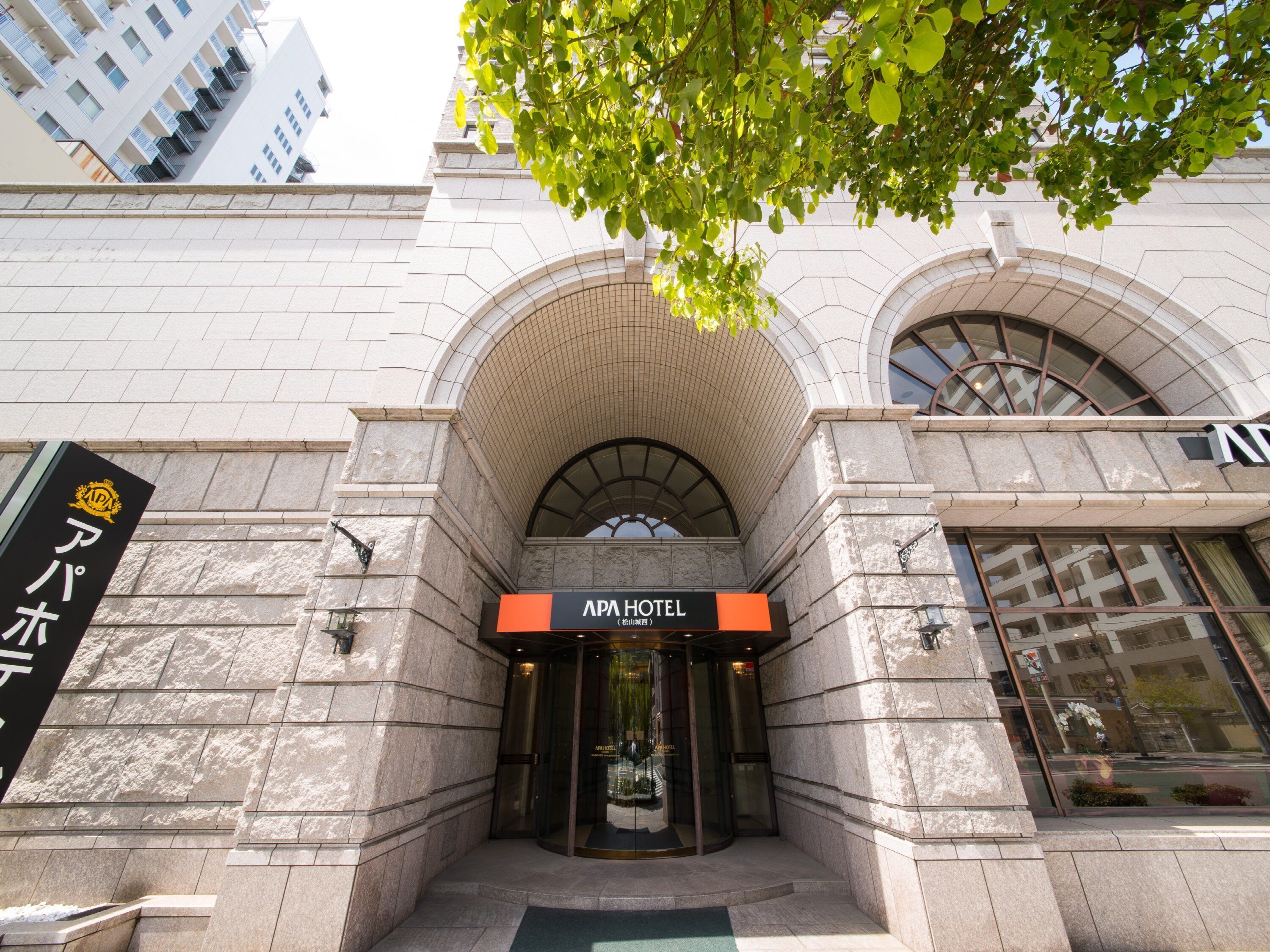 The entrance of APA Hotel with a stone facade and arched windows.