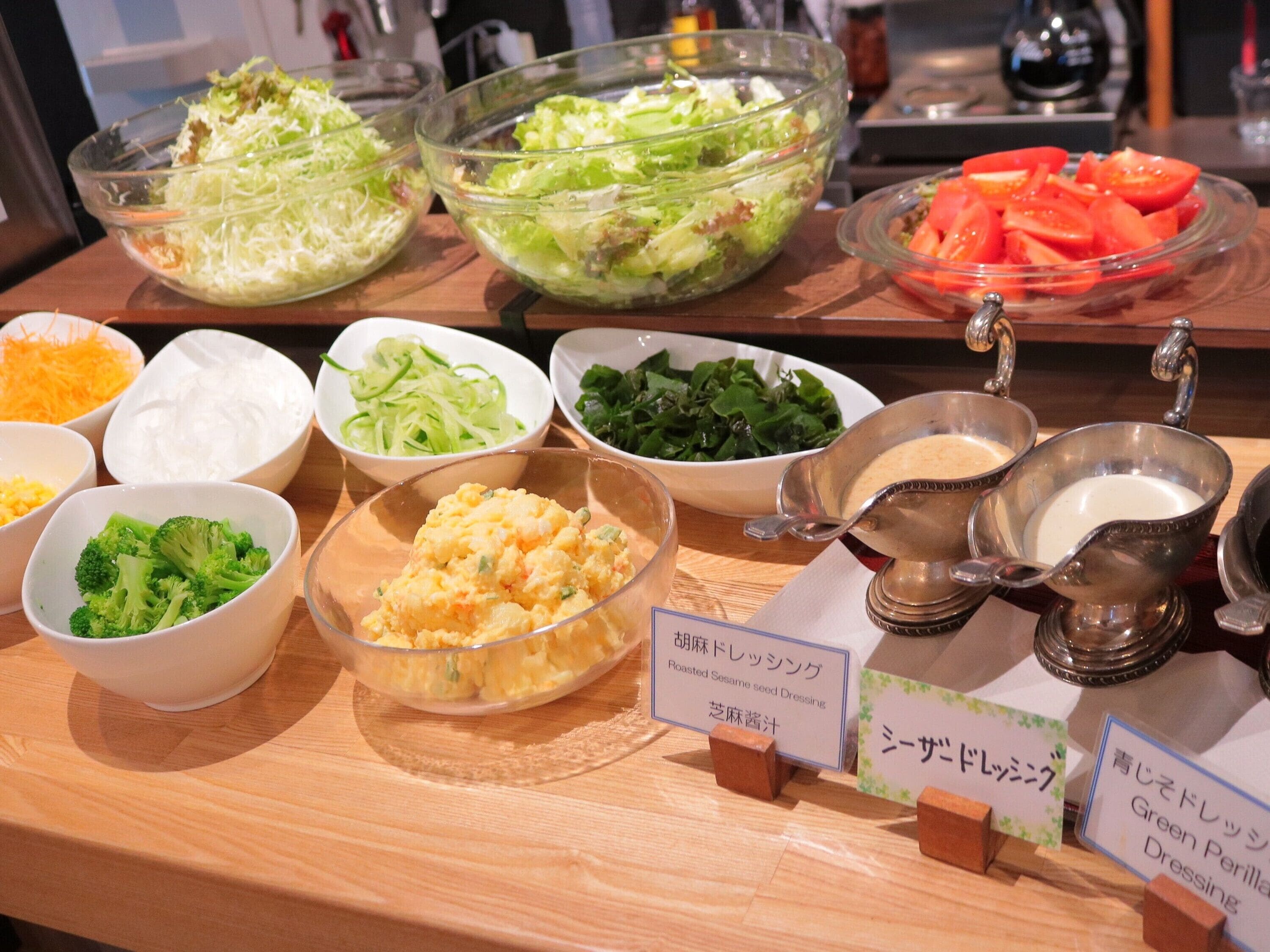 Un bufé con diversos platos, incluyendo ensaladas, verduras y aderezos.