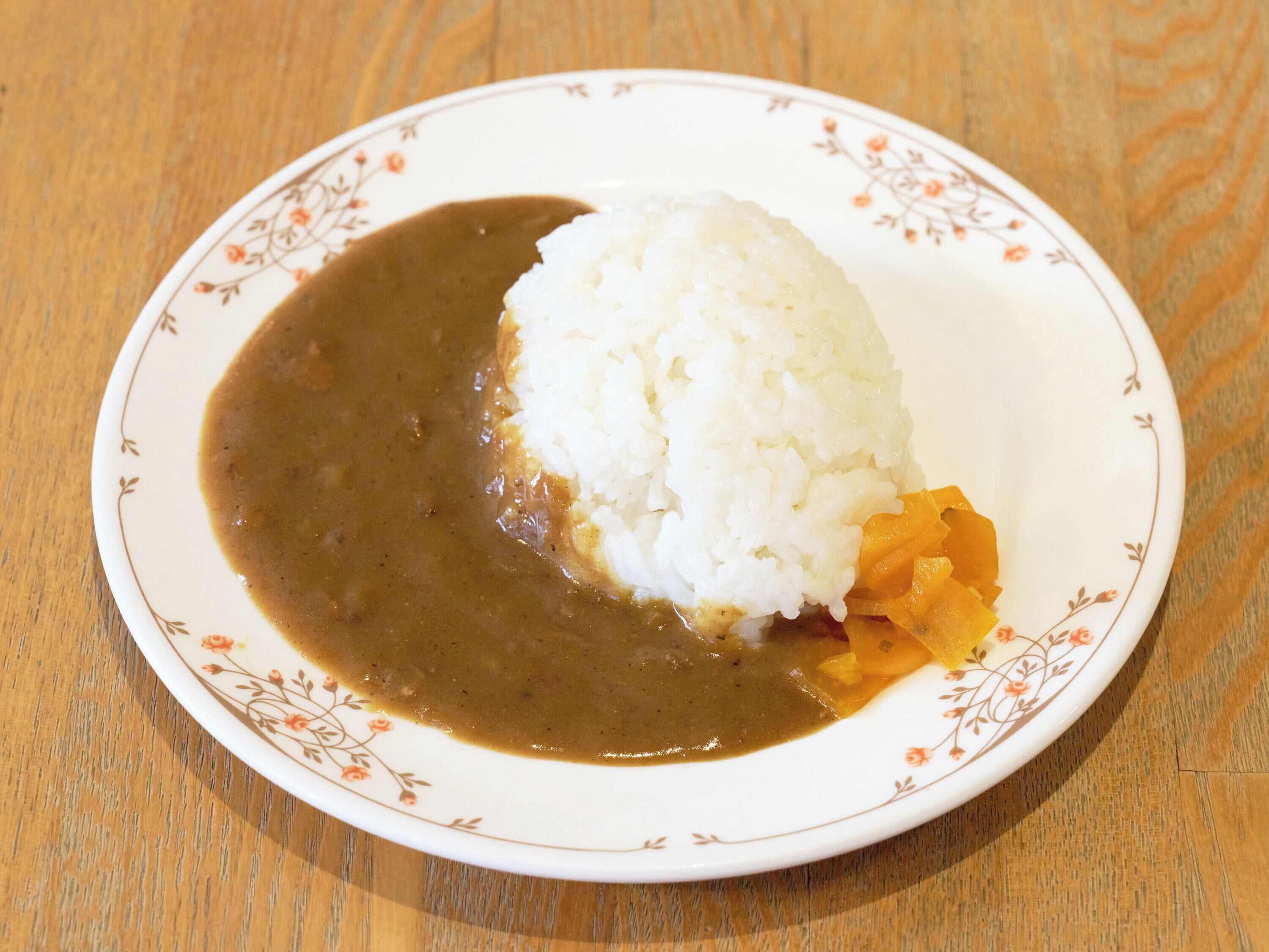 A plate with white rice and a brown sauce, possibly curry, on a floral-patterned plate.