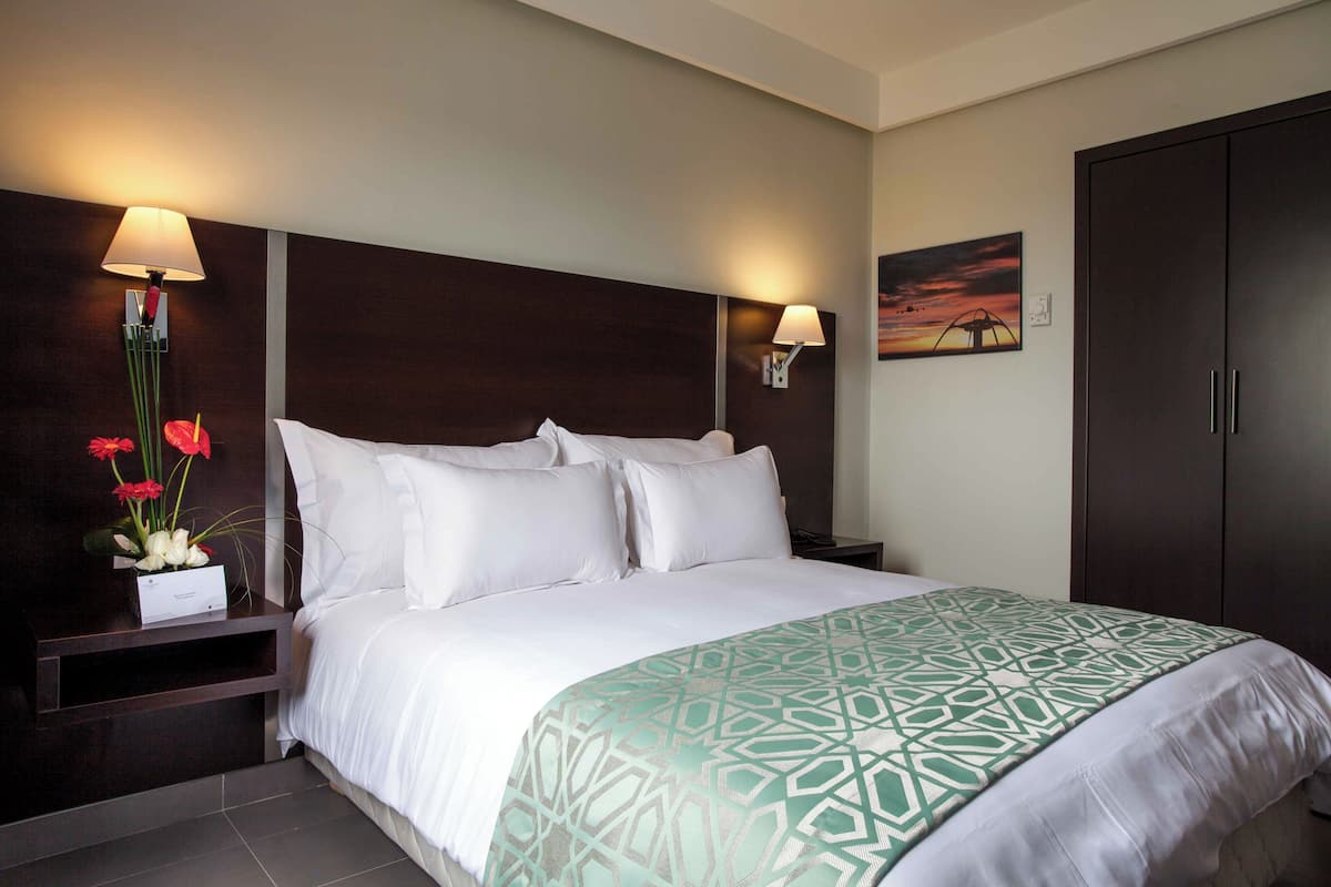 Quarto de hotel com uma cama grande, duas luminárias de cabeceira, uma mesa de cabeceira com um vaso de flores e um guarda-roupa.