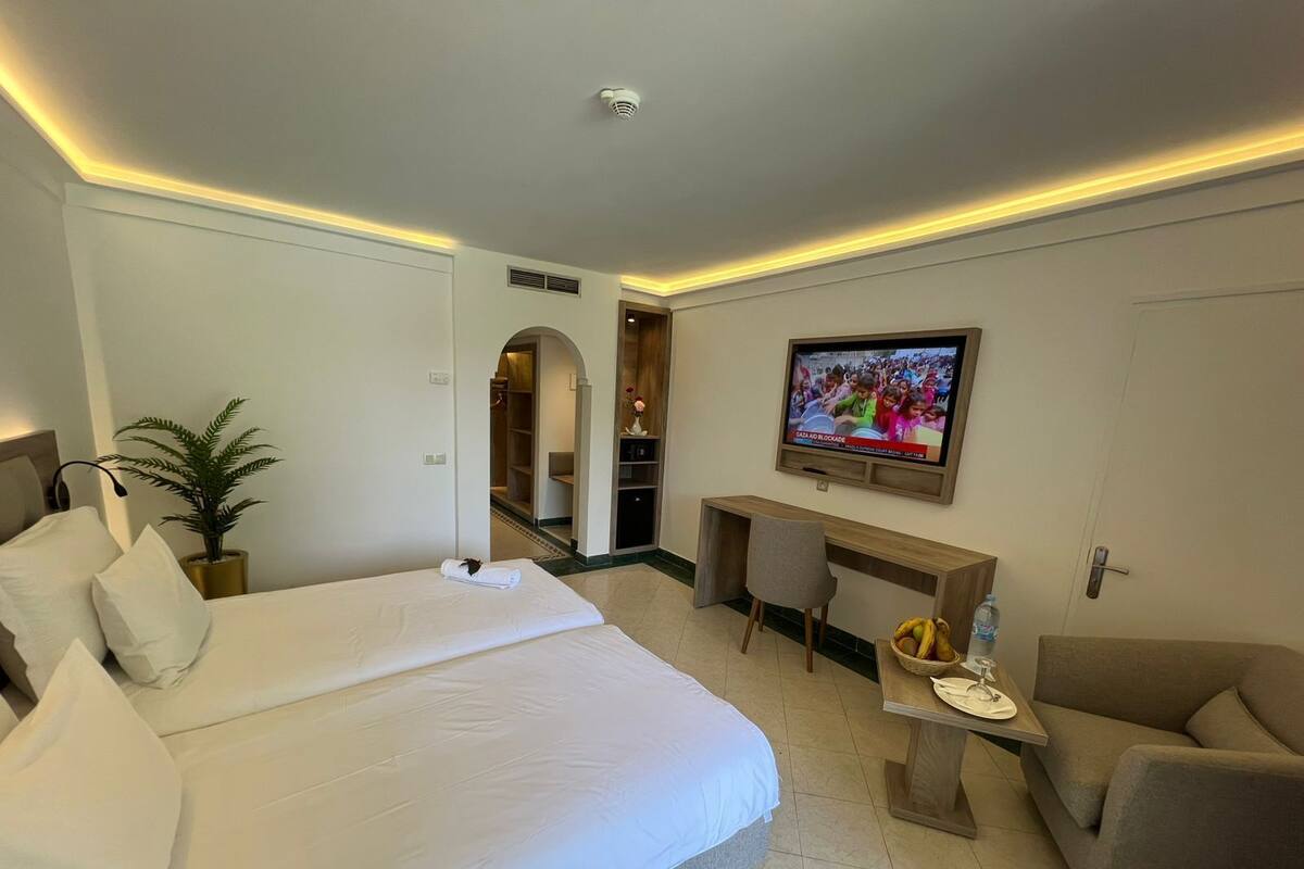Quarto de hotel com uma cama grande, uma escrivaninha, uma televisão e um espaço para sentar.