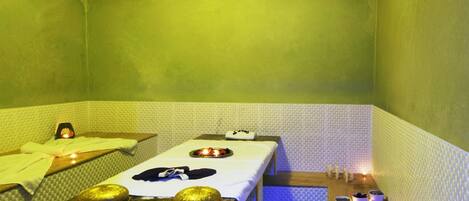 A small, dimly lit room with a single bed, a small table with a tray of food, and a wall-mounted heater.