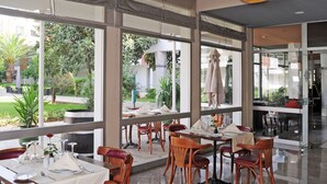 A restaurant with large windows, wooden chairs, and tables set for dining. - Hôtel Volubilis (Fes)
