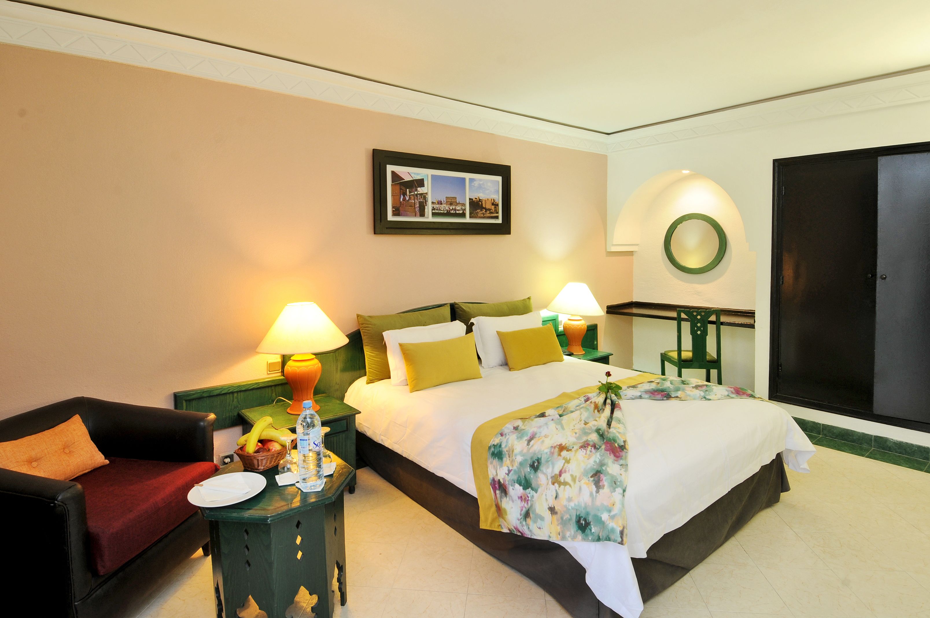 Une chambre d’hôtel avec un lit, un canapé, une table avec une lampe, un tableau accroché au mur et une porte.