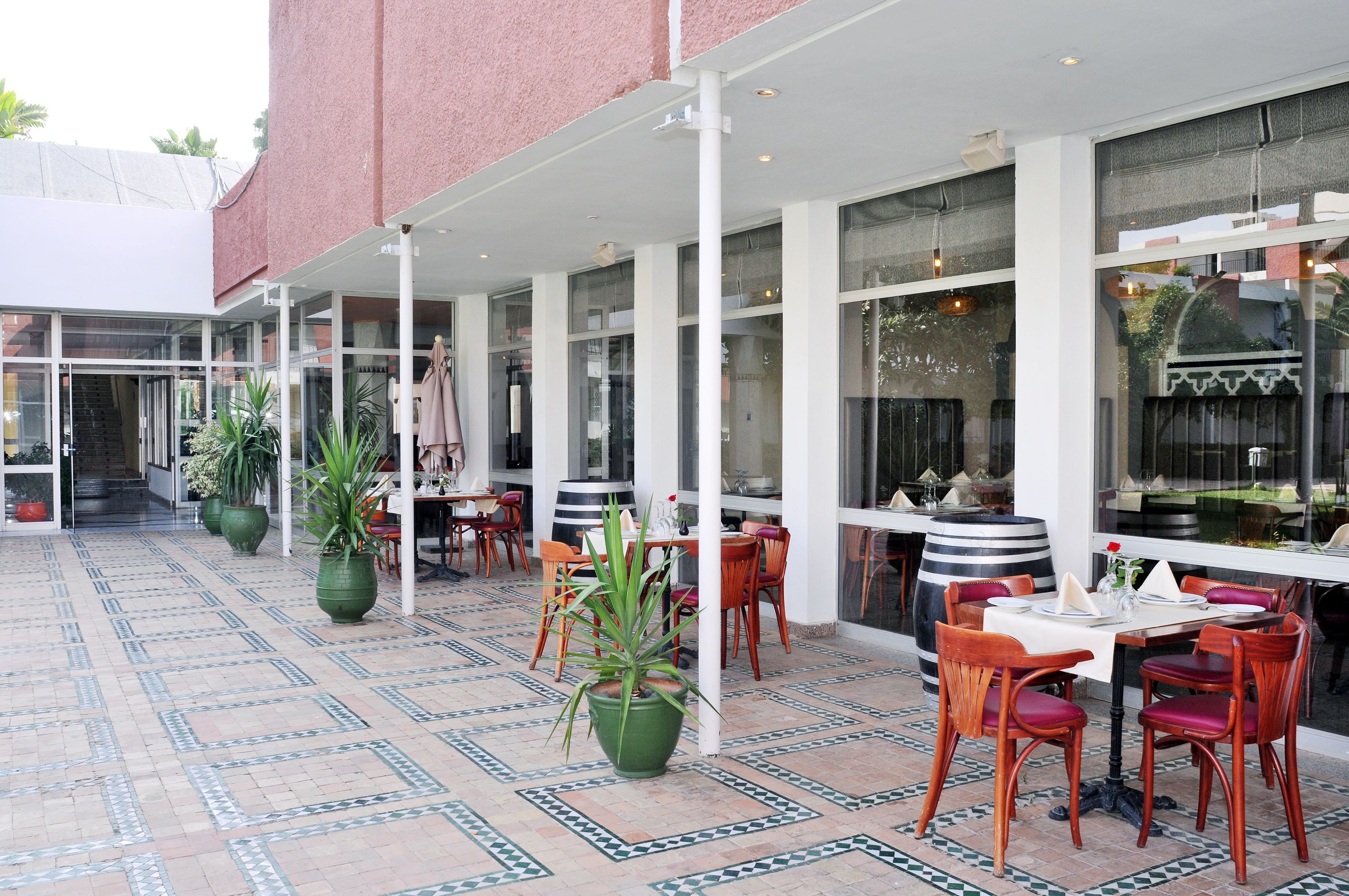 An outdoor cafe area with tables and chairs, potted plants, and a tiled floor.