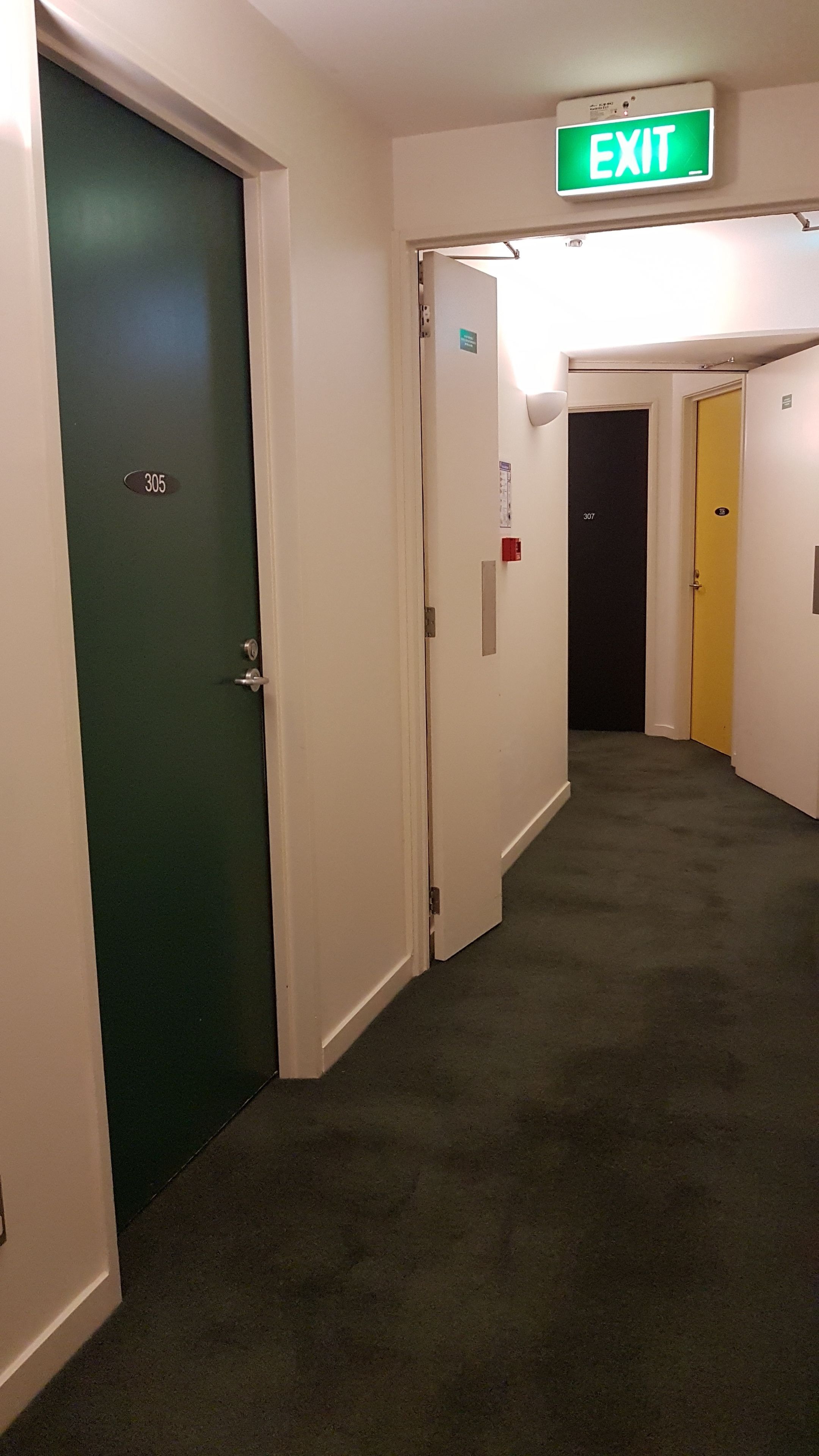 A hallway with doors numbered 305 and 307, an exit sign, and a yellow door.