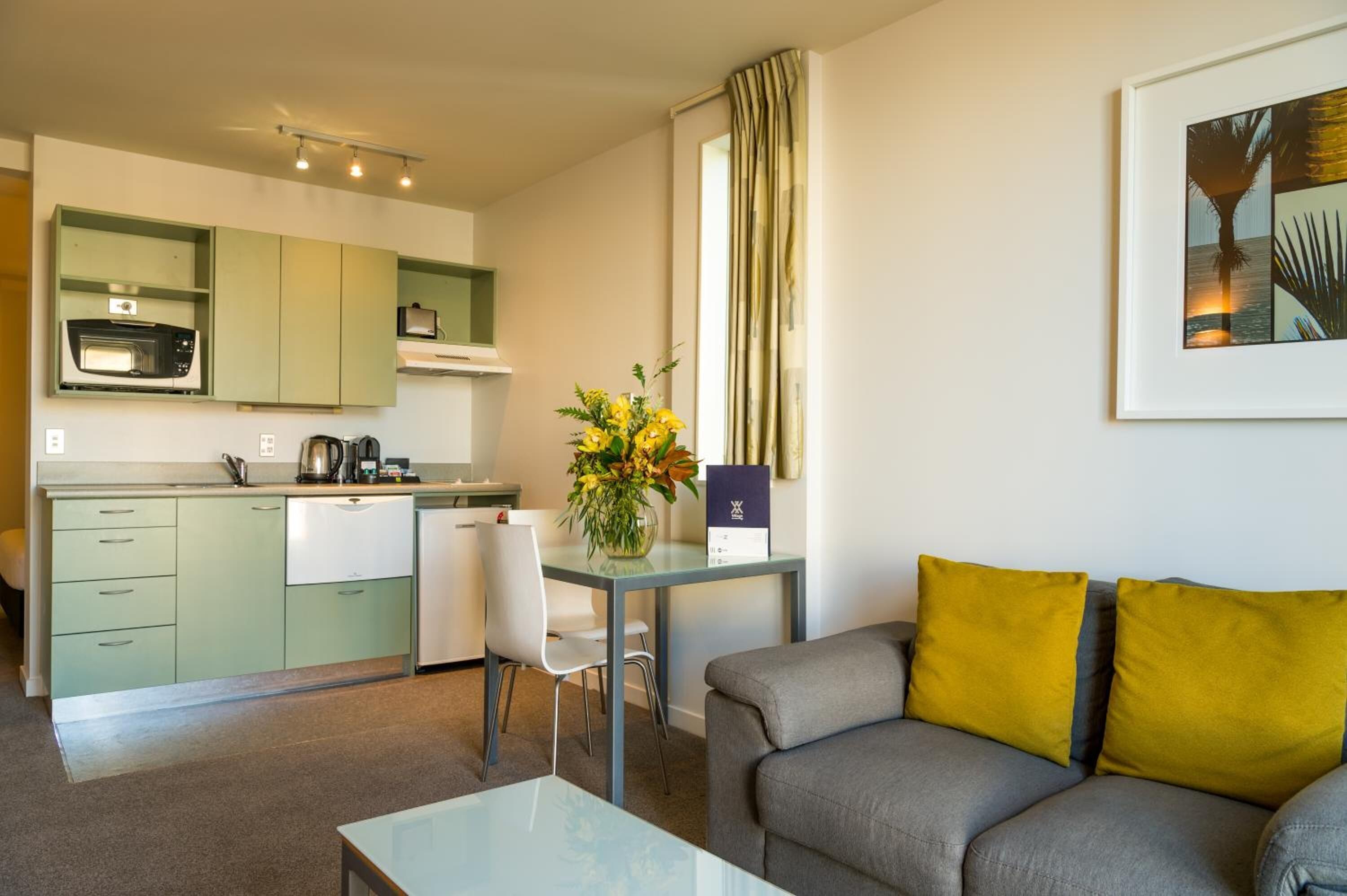 A compact living space with a kitchenette, a dining area, and a sofa with yellow cushions.