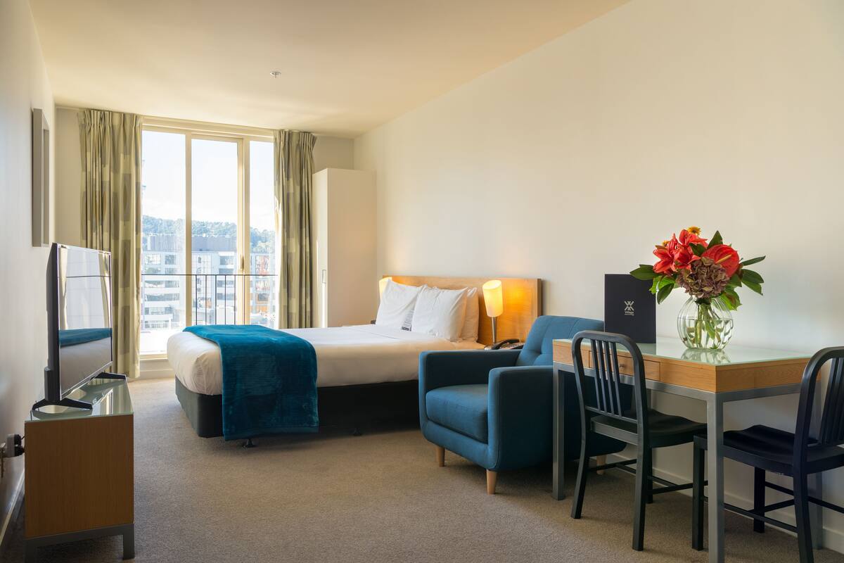 Een hotelkamer met een bed, een bureau, een stoel, een televisie en een raam met gordijnen.