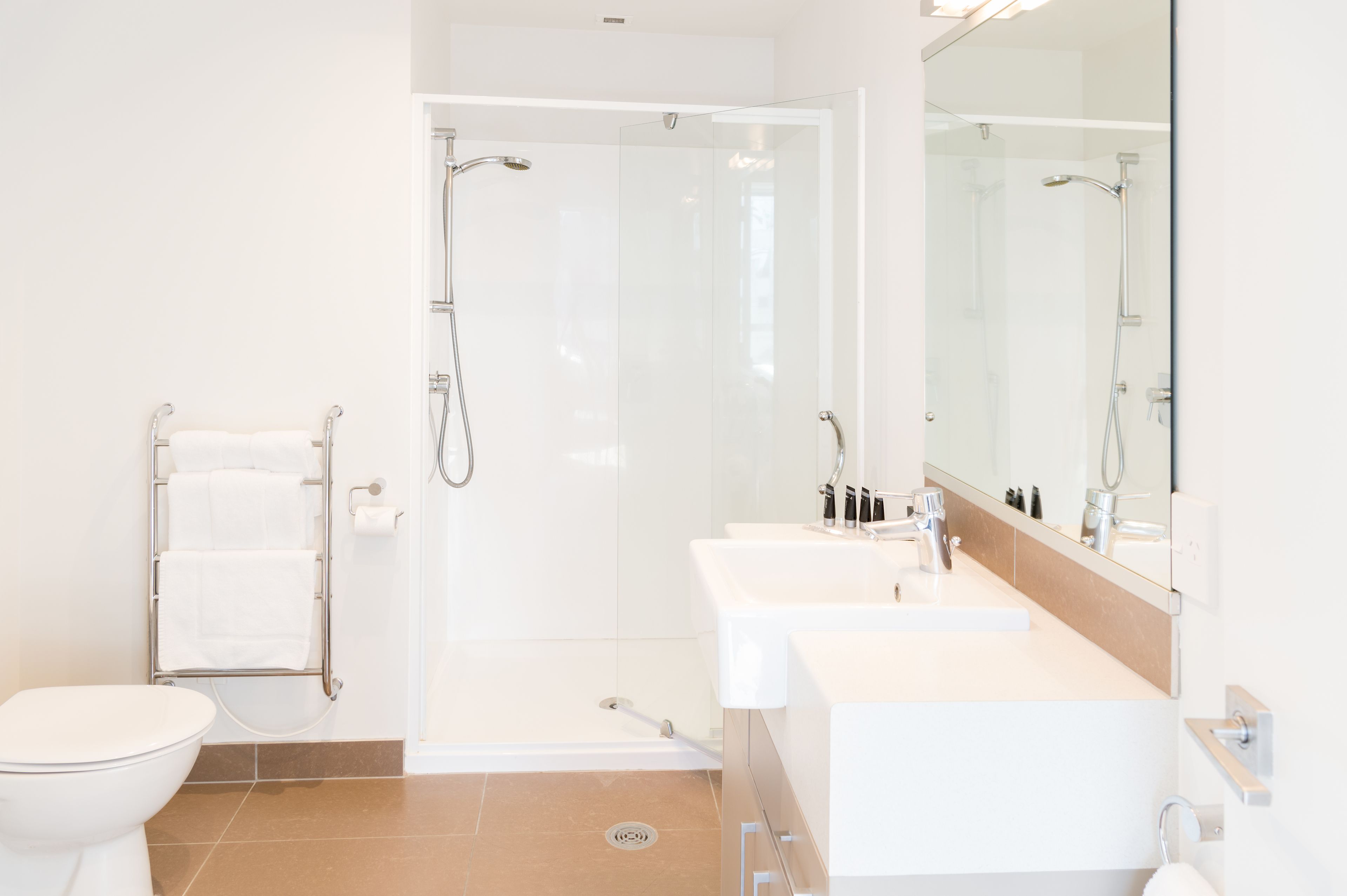 Un baño moderno con ducha a ras de suelo, inodoro y tocador con espejo.