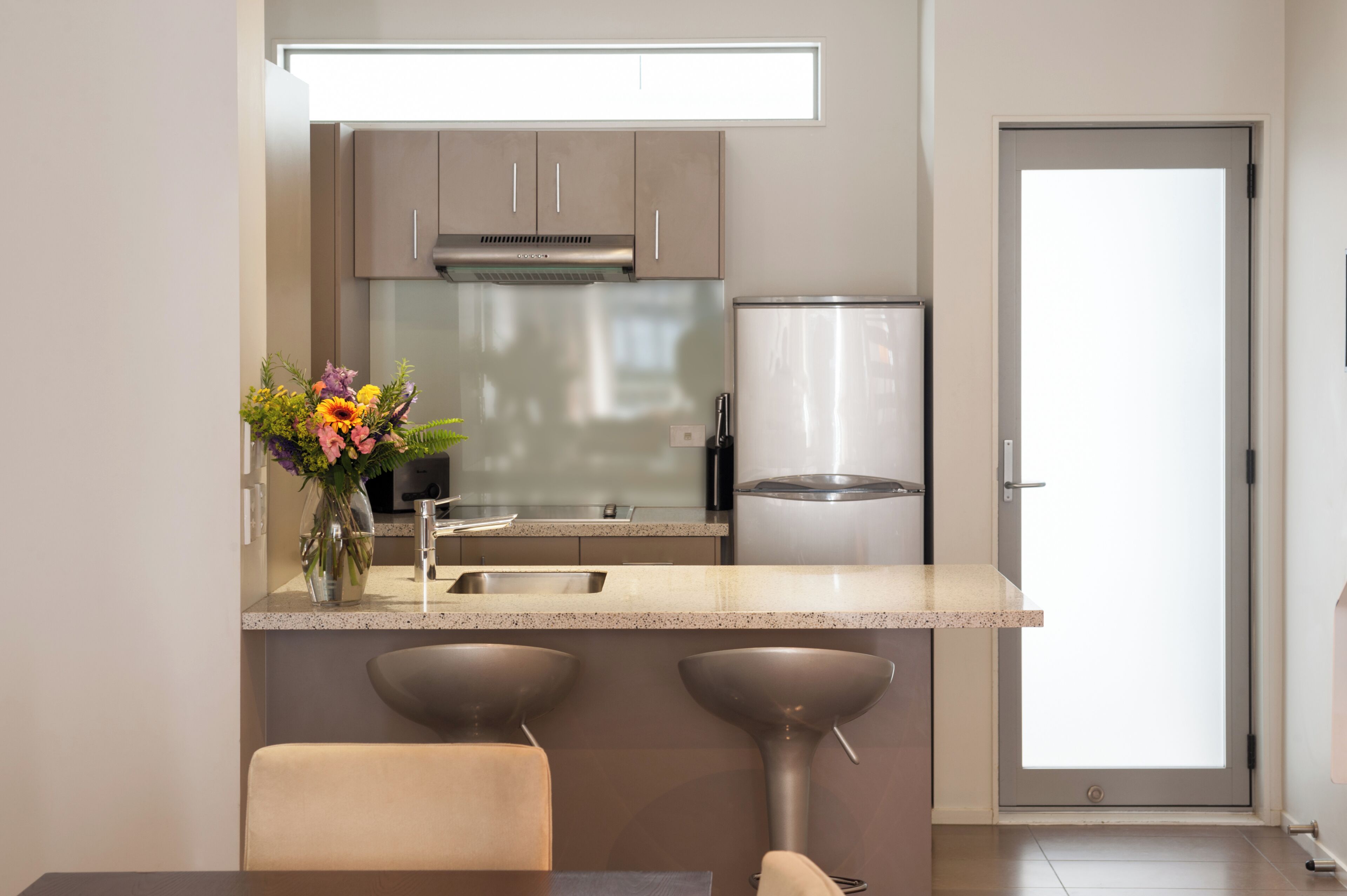 Una cocina moderna con electrodomésticos de acero inoxidable, encimera de mármol y un florero con flores.