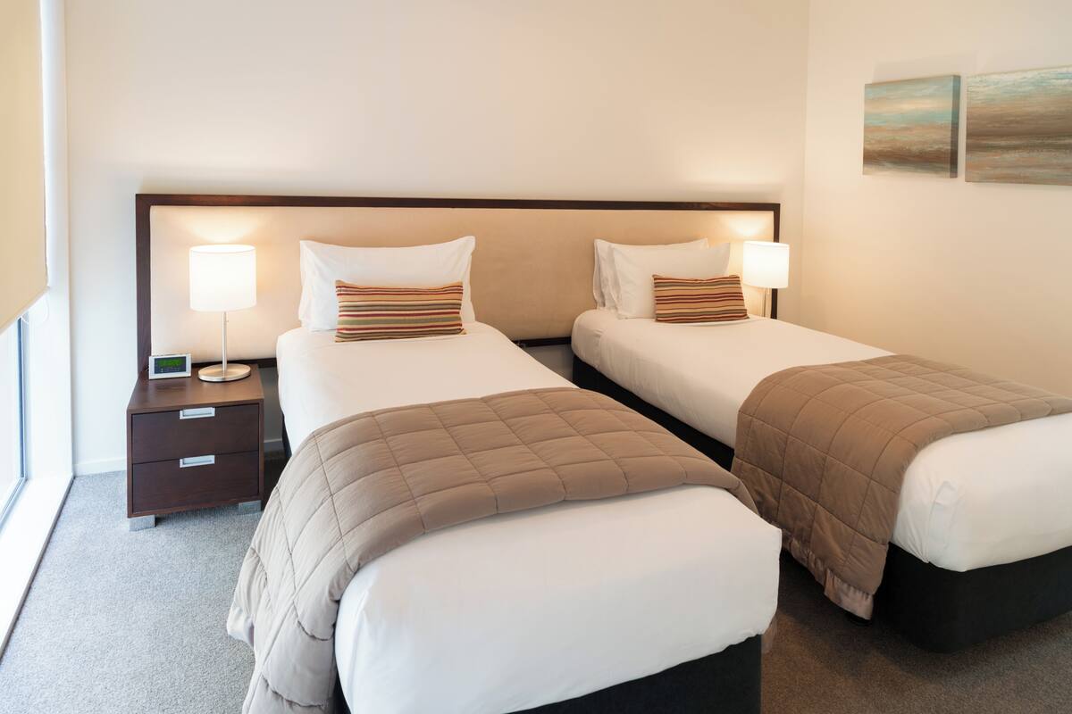 Une chambre d’hôtel avec deux lits, chacun doté d’une tête de lit, de tables de chevet et de lampes.
