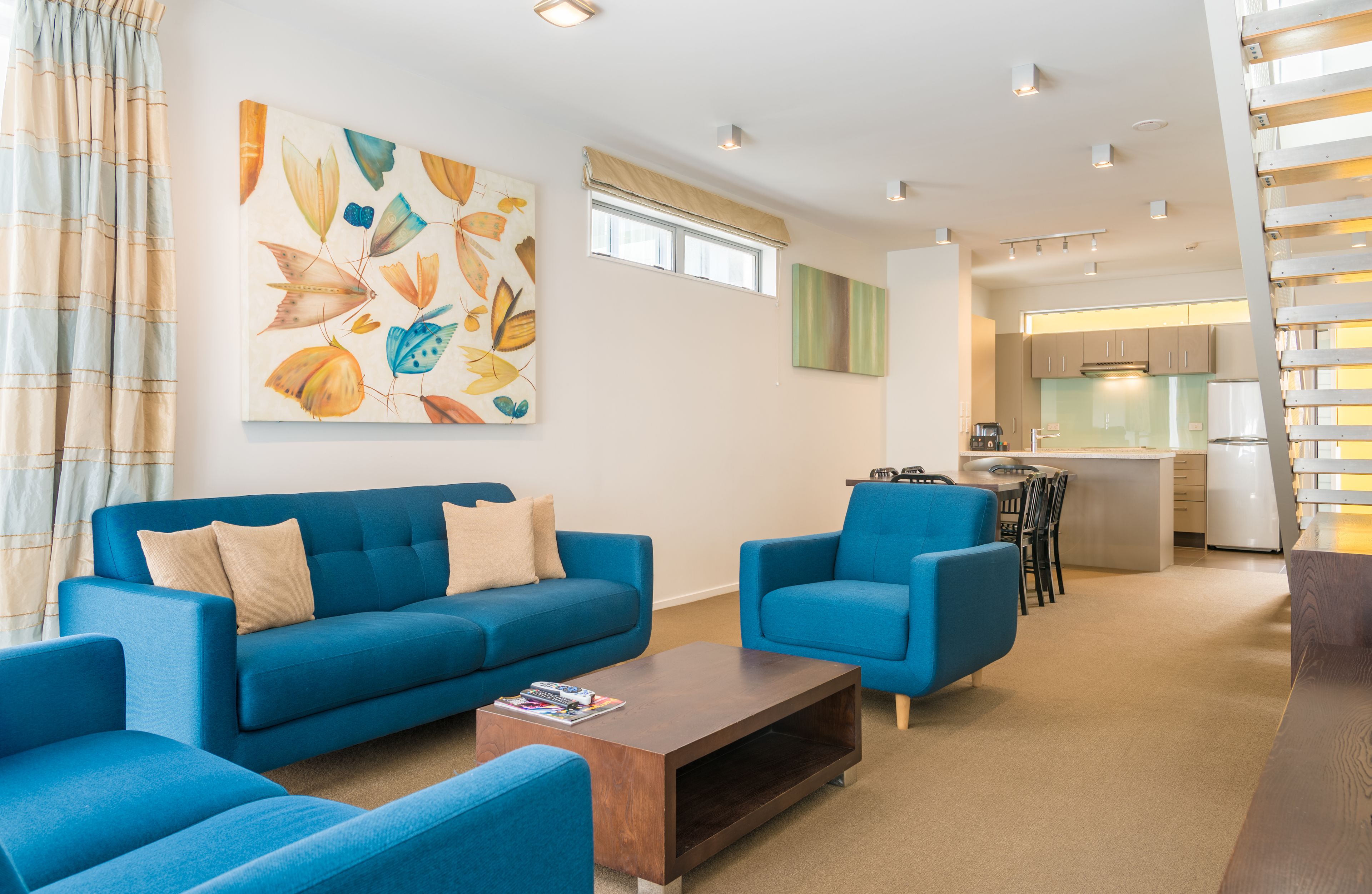 A modern living room with a blue sofa set, a coffee table, and a large abstract painting on the wall.