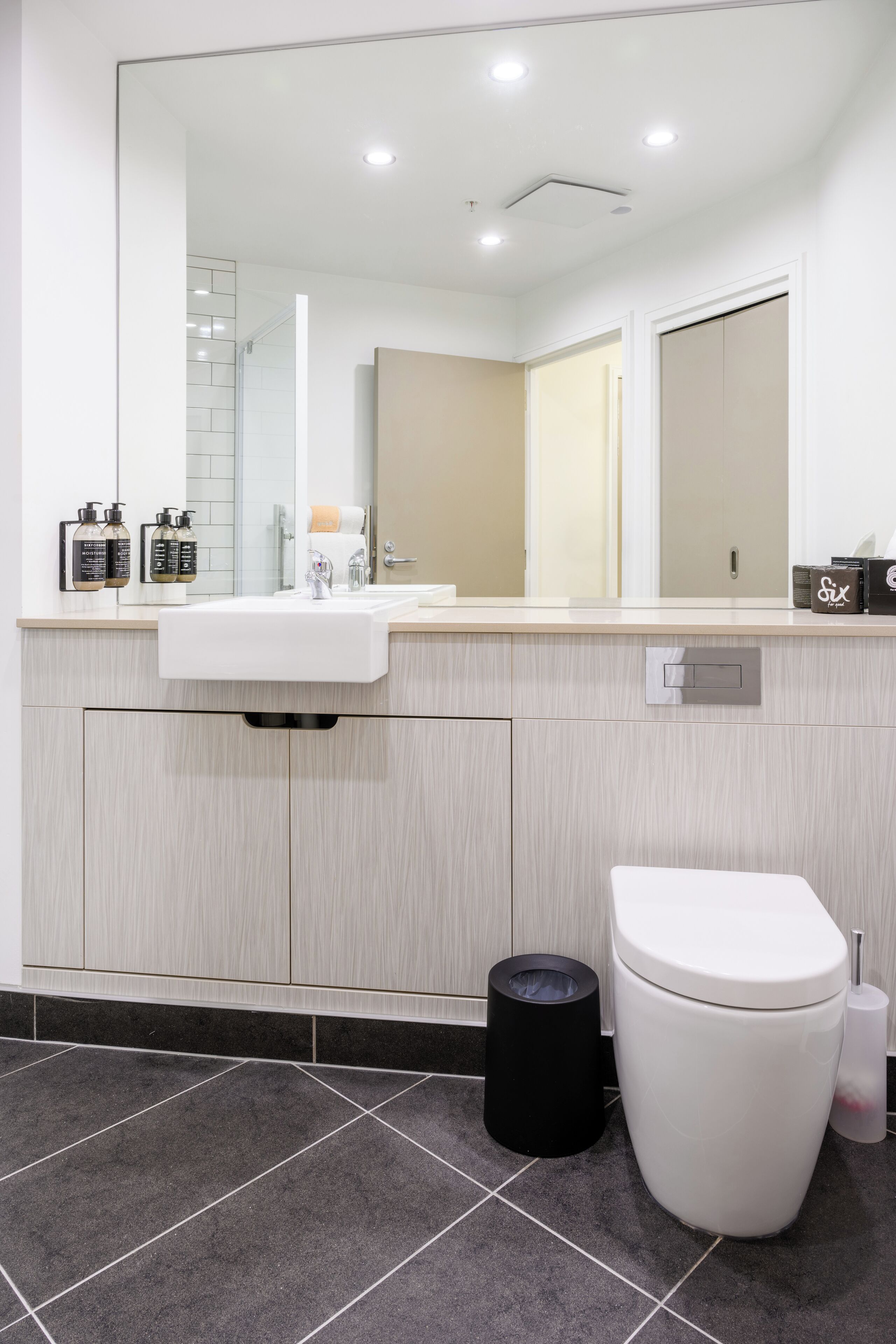 A modern bathroom with a large mirror, a sink, and a toilet.