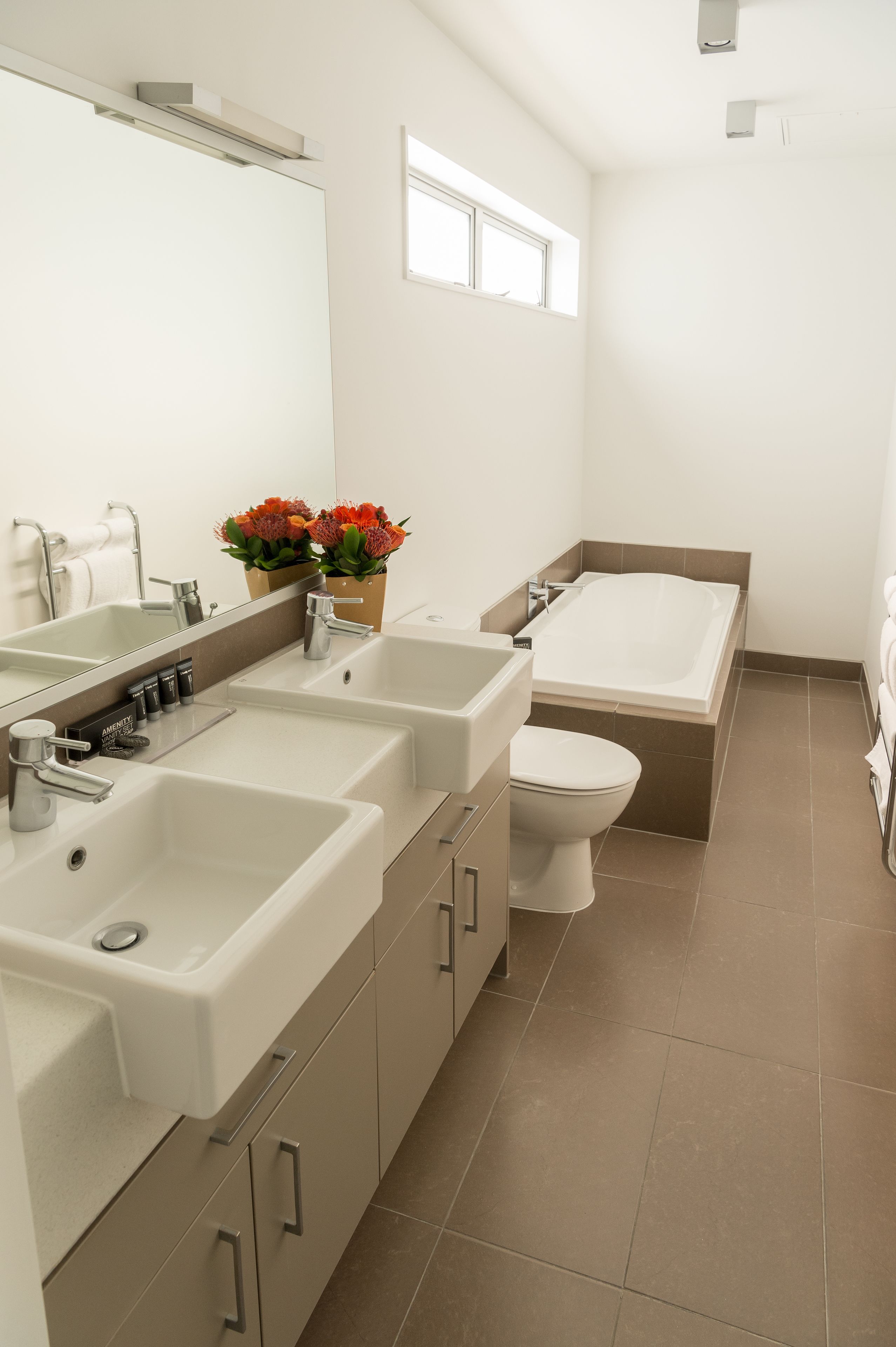 A modern bathroom with a large sink, a bathtub, and a toilet. There are two sinks and a mirror above them.