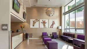 A reception area with a counter, purple seating, giraffe artwork, and large windows. - Boulcott Suites (Wellington)