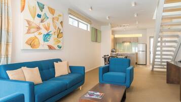 Un salon moderne avec un canapé bleu, un fauteuil assorti et une table basse en bois. Un tableau abstrait aux couleurs vives orne le mur.