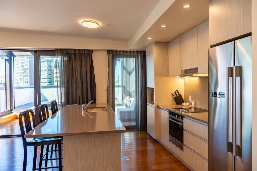 Una cocina moderna con una isla central, electrodomésticos de acero inoxidable y ventanas grandes con cortinas.