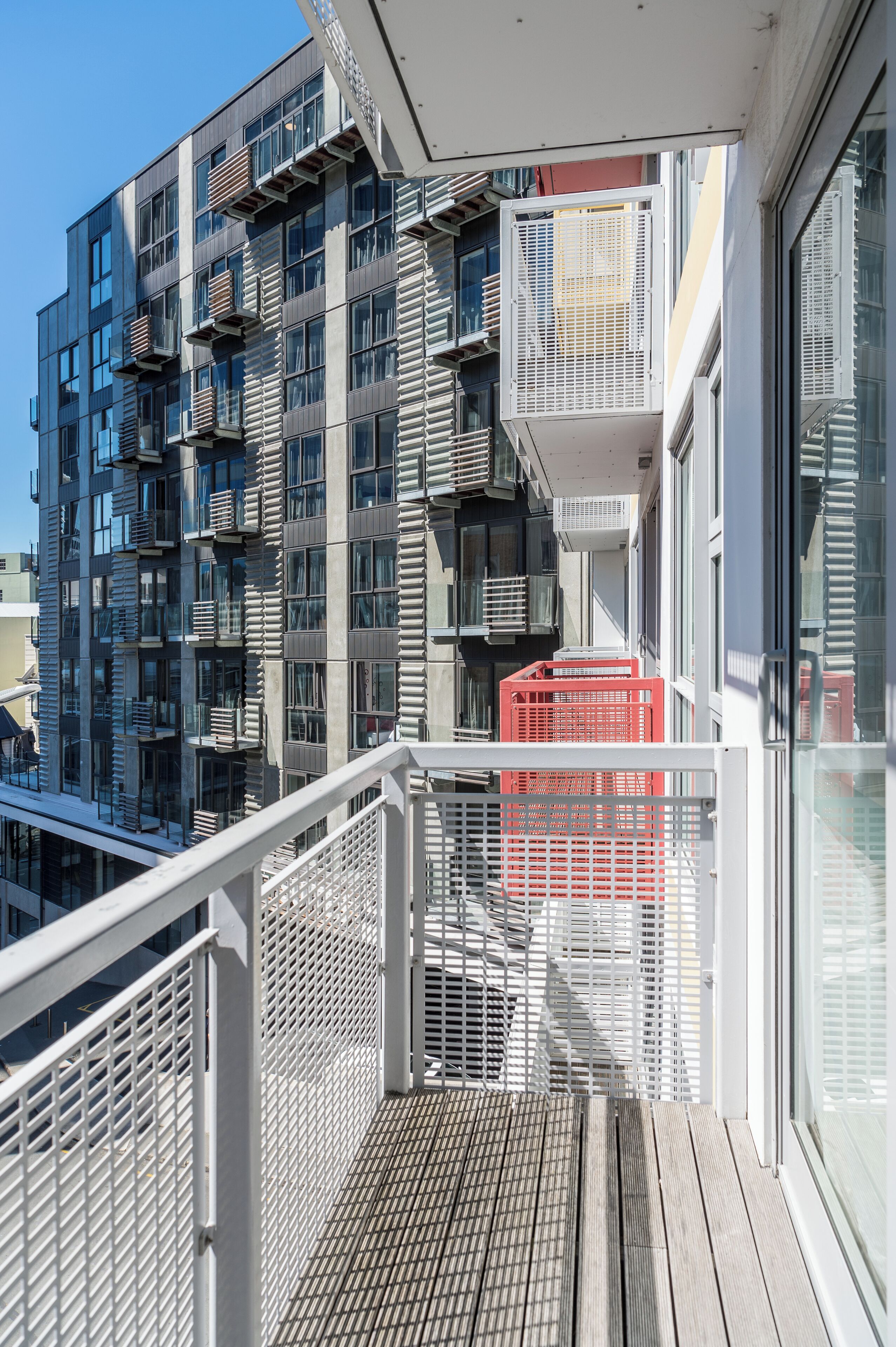 A modern building with multiple balconies, large windows, and a wooden deck.