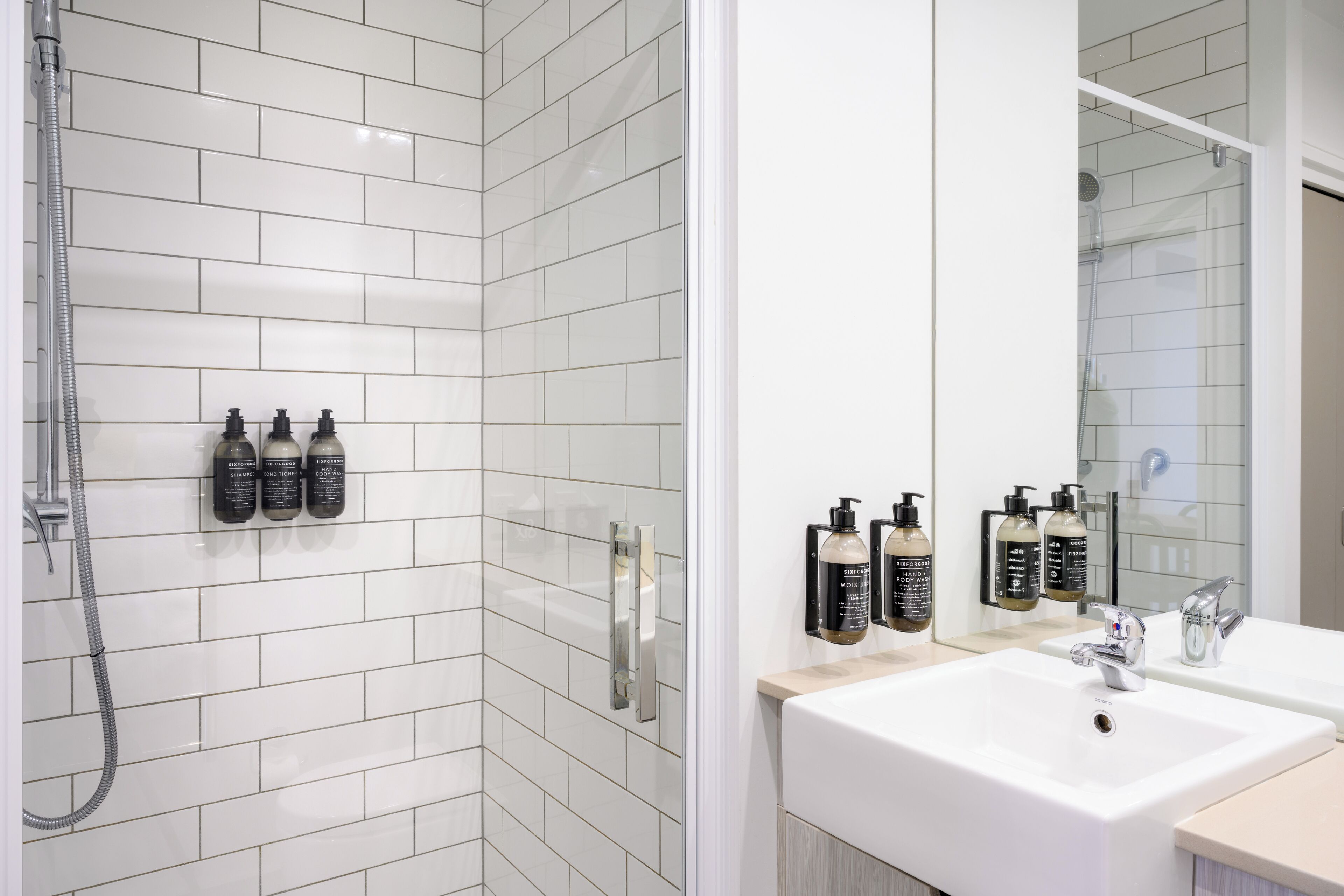 A modern bathroom with white tiled walls, a glass shower enclosure, and two sinks with faucets.