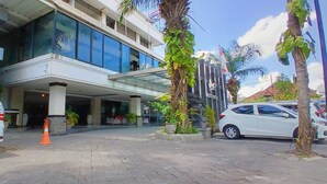 A modern building with a glass facade, a parking area, and a few potted plants. - Nirmala Hotel and Convention Centre (Denpasar)