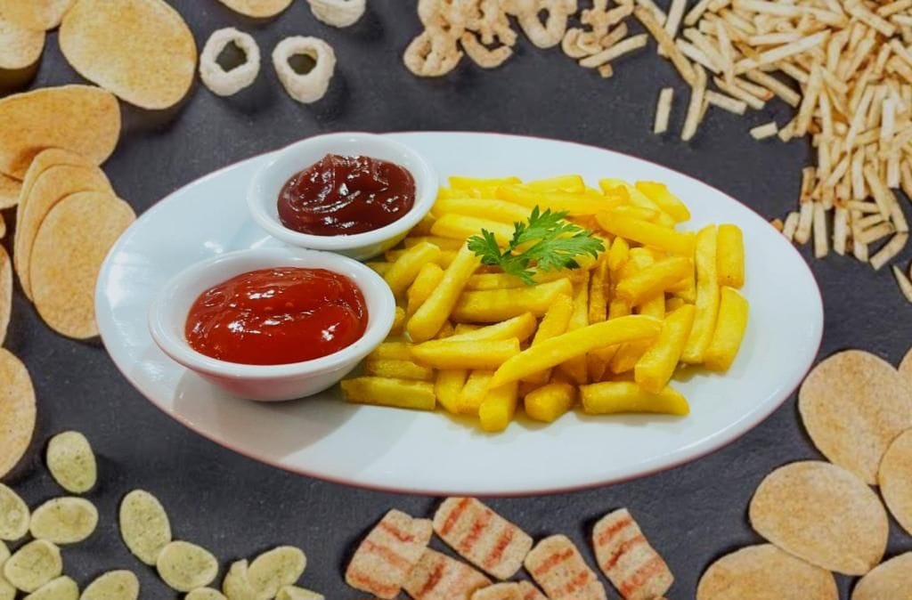 A plate of French fries with ketchup and a parsley garnish, surrounded by potato chips and onion rings.