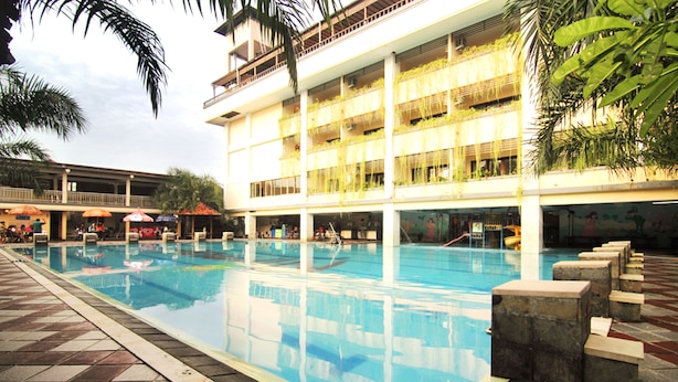 A large indoor swimming pool with multiple lanes, surrounded by a tiled deck and a multi-story building with balconies. - Nirmala Hotel and Convention Centre (Denpasar)