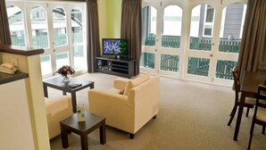 A living room with a sofa, a coffee table, a TV, and a balcony with a view. - Willis Village (Wellington)