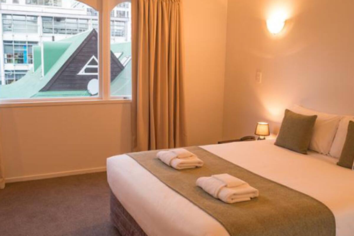 A hotel room with a bed, curtains, a window, and a nightstand with a lamp.