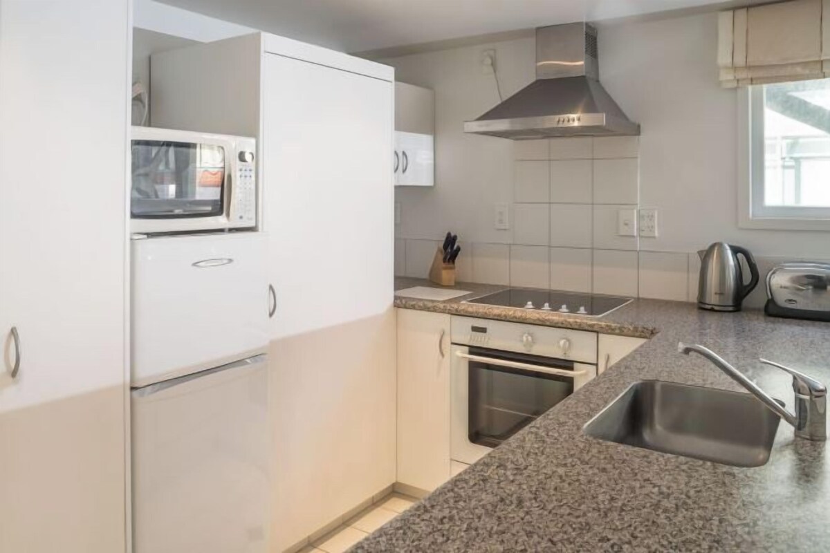 Una cocina con armarios blancos, microondas, estufa, fregadero y ventana.