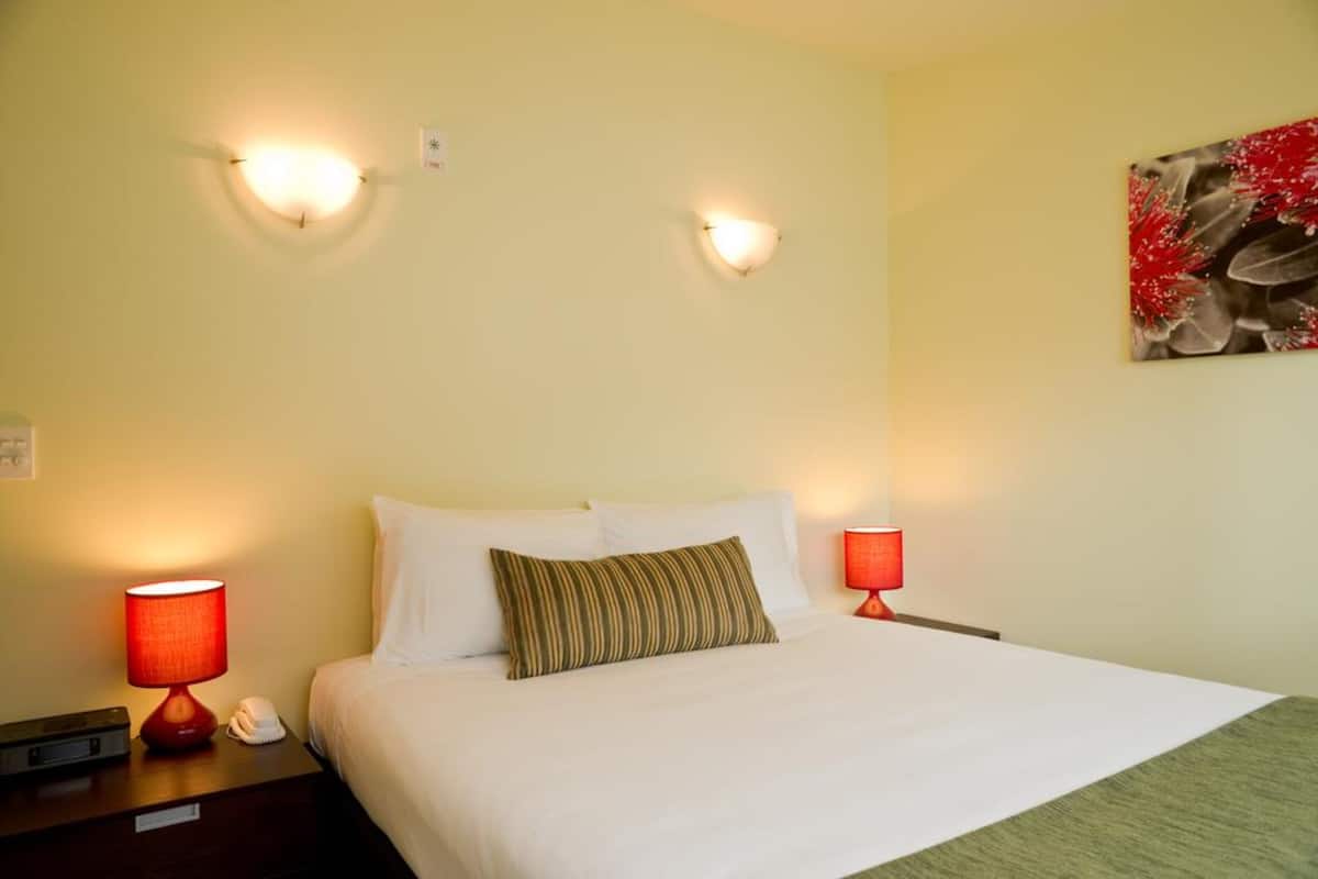 A hotel room with a bed, two bedside lamps, a telephone, and a wall-mounted artwork.