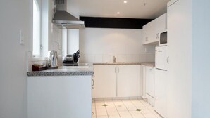 A modern kitchen with white cabinets, a microwave, and a stove. - Willis Village (Wellington)